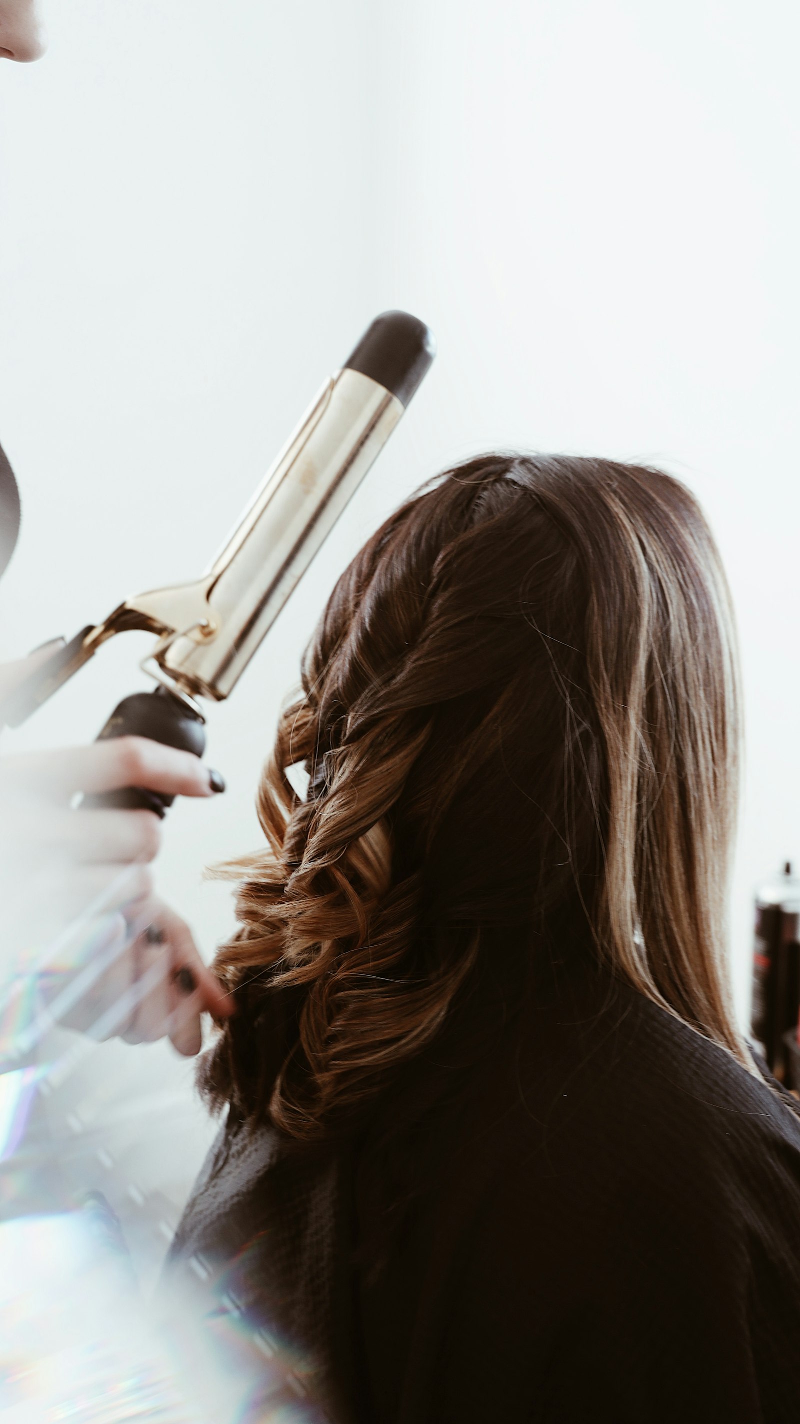 A stylist using a gold barrel curling iron on long brown hair