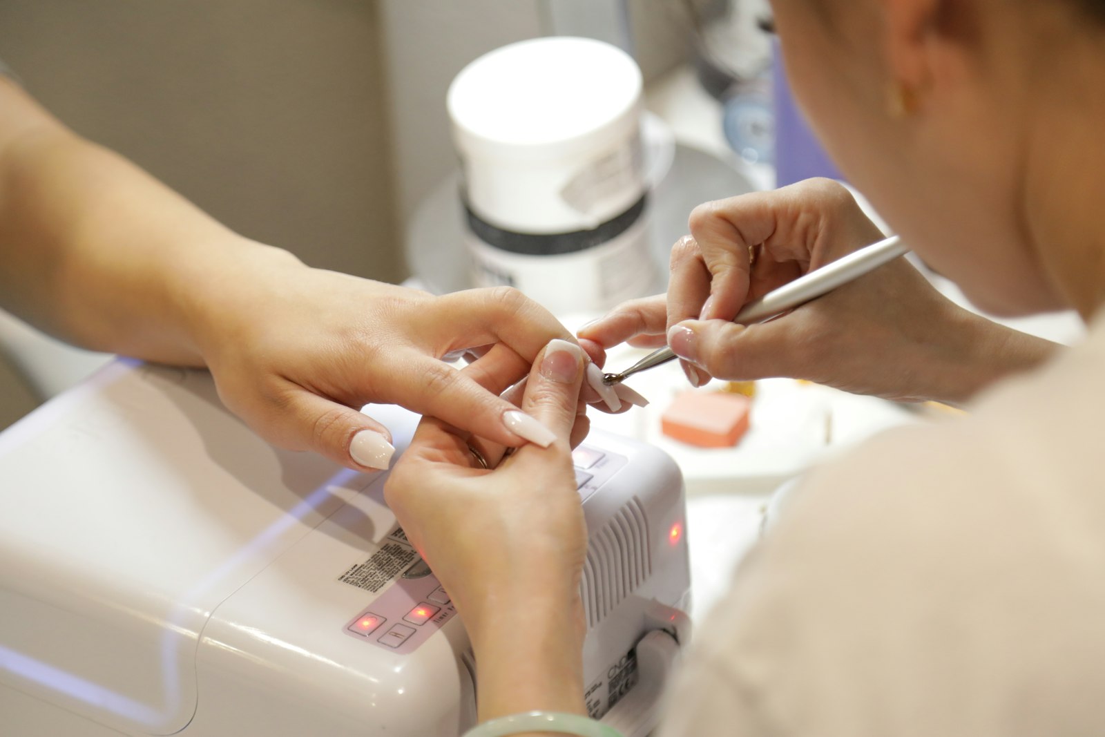 A nail technician curing a client's gel manicure under a white LED nail lamp