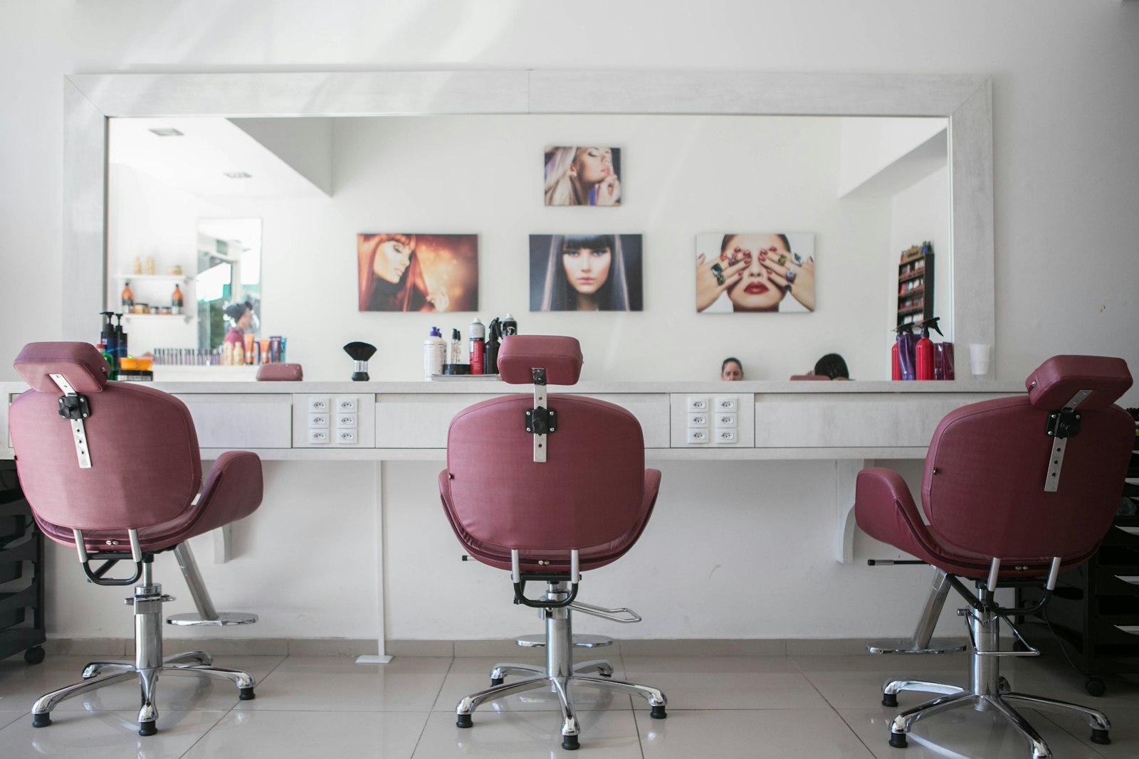 Interior of a hair salon with three empty pink styling chairs facing a long mirror