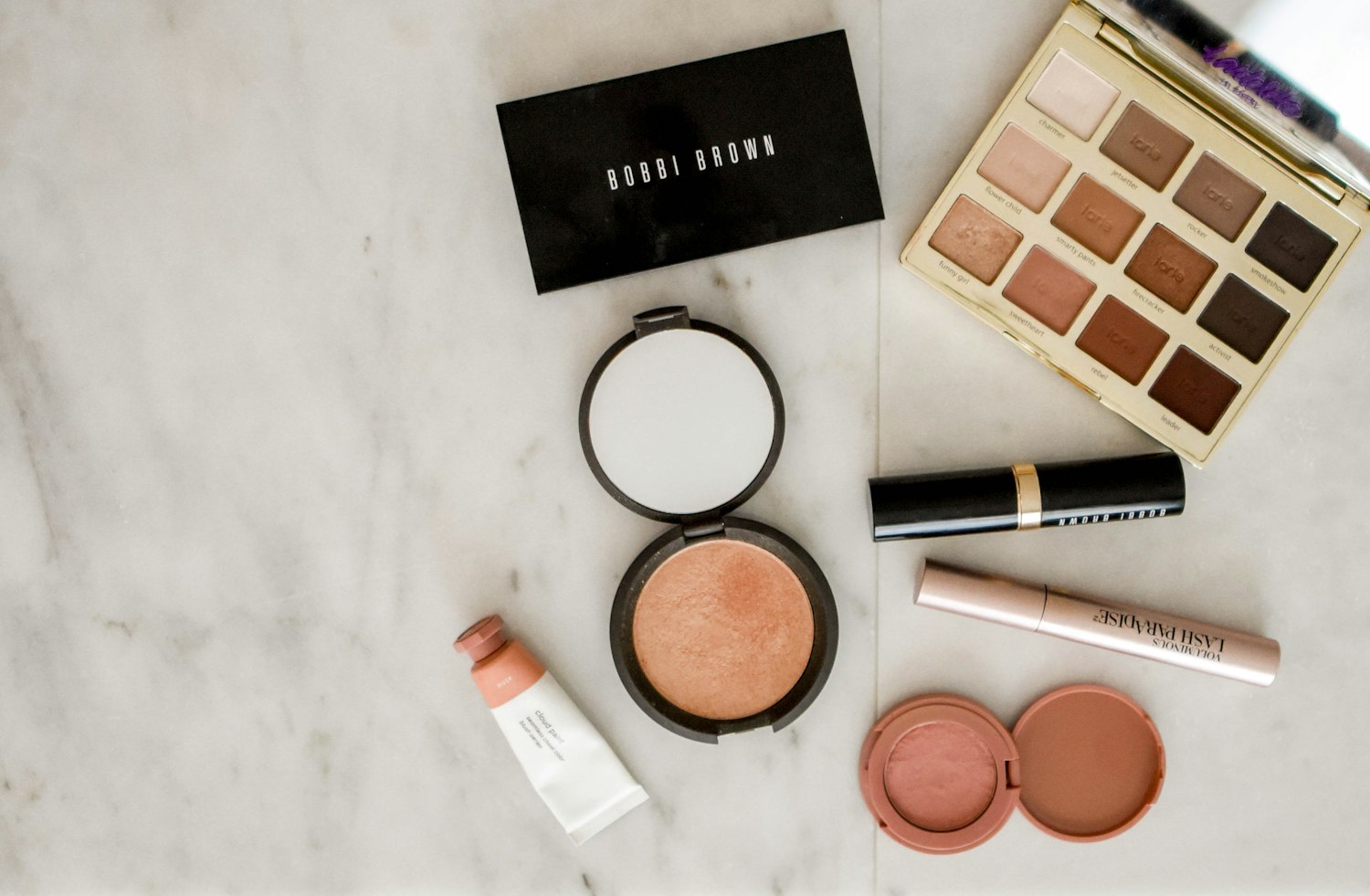 Makeup products including a compact, eyeshadow palette and lip colour arranged on a marble surface