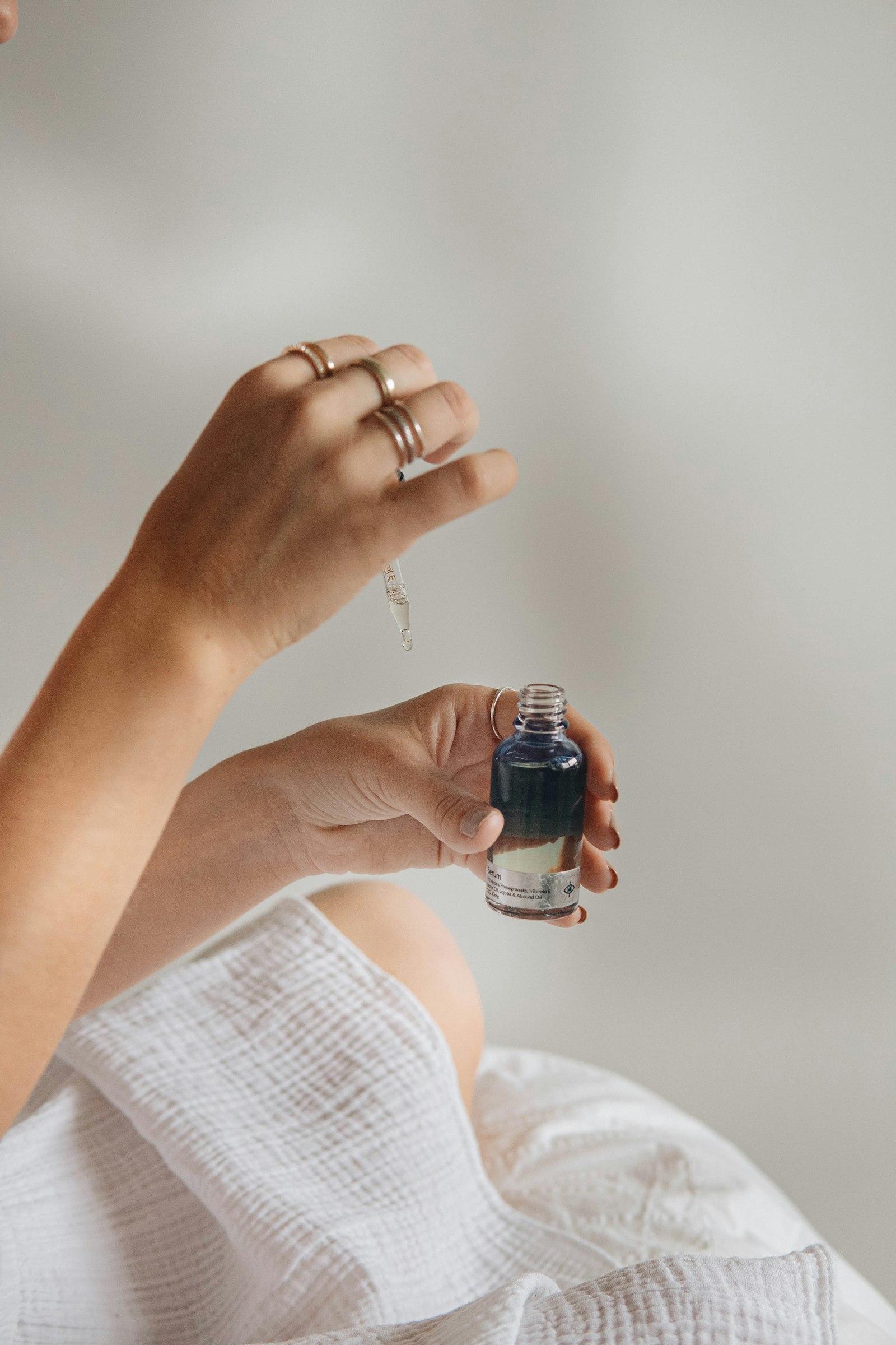A hand holding a dropper above a small bottle of dark blue serum