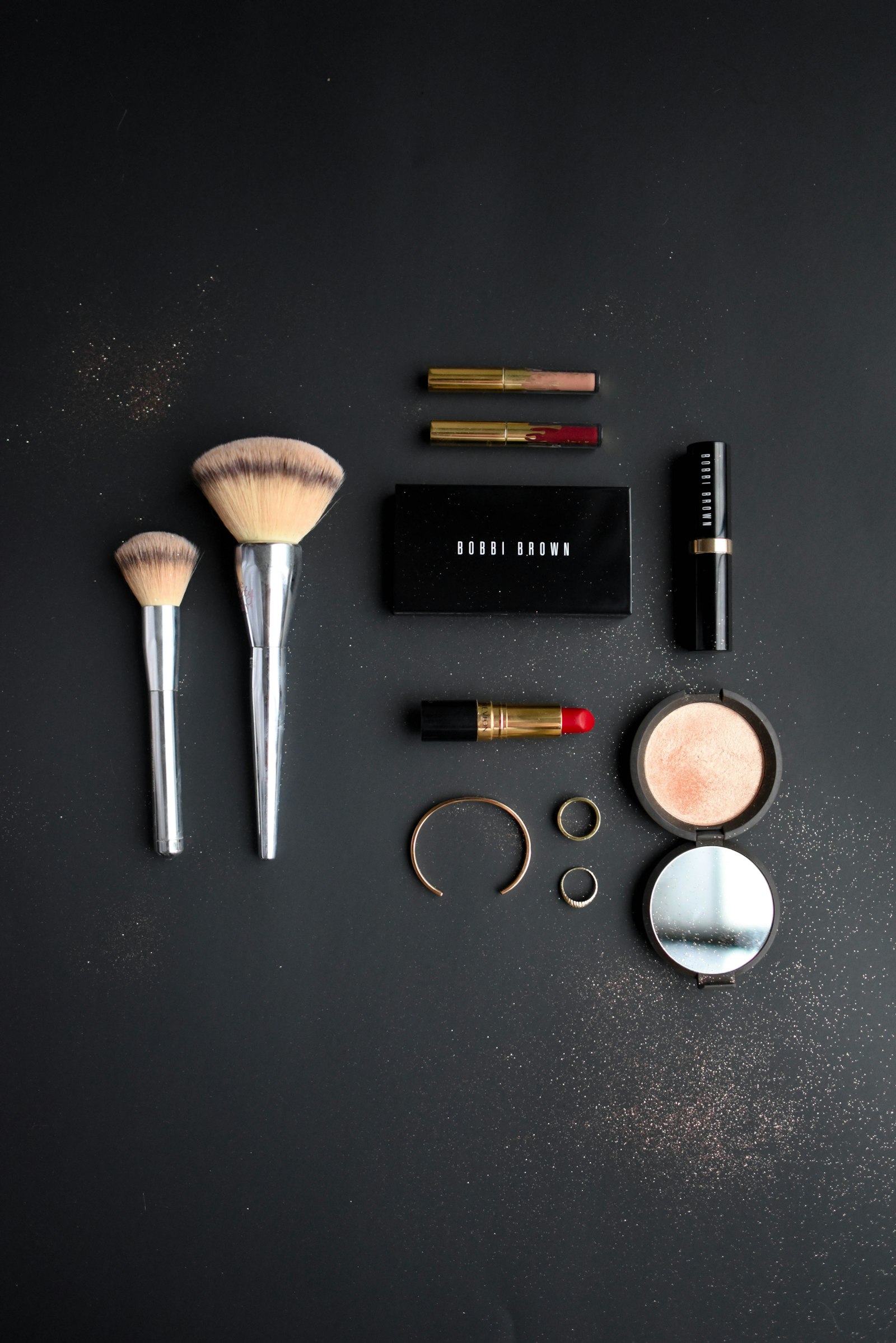 Makeup brushes, compacts and lipsticks arranged neatly on a dark slate surface