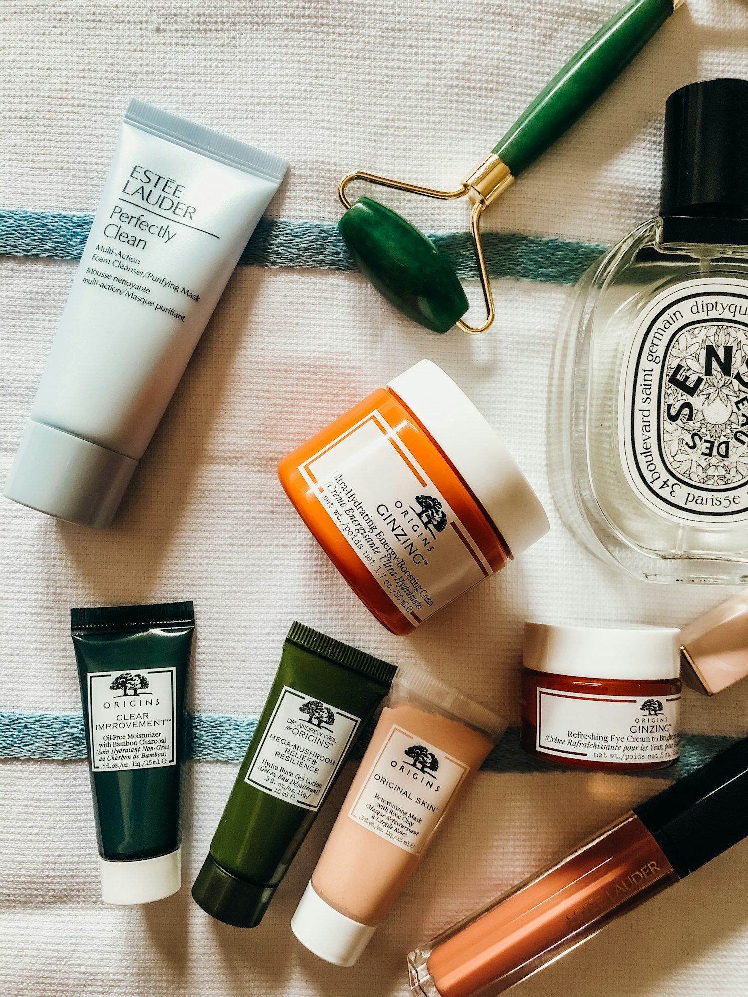 Skincare and fragrance products including a jade roller arranged on a striped textile
