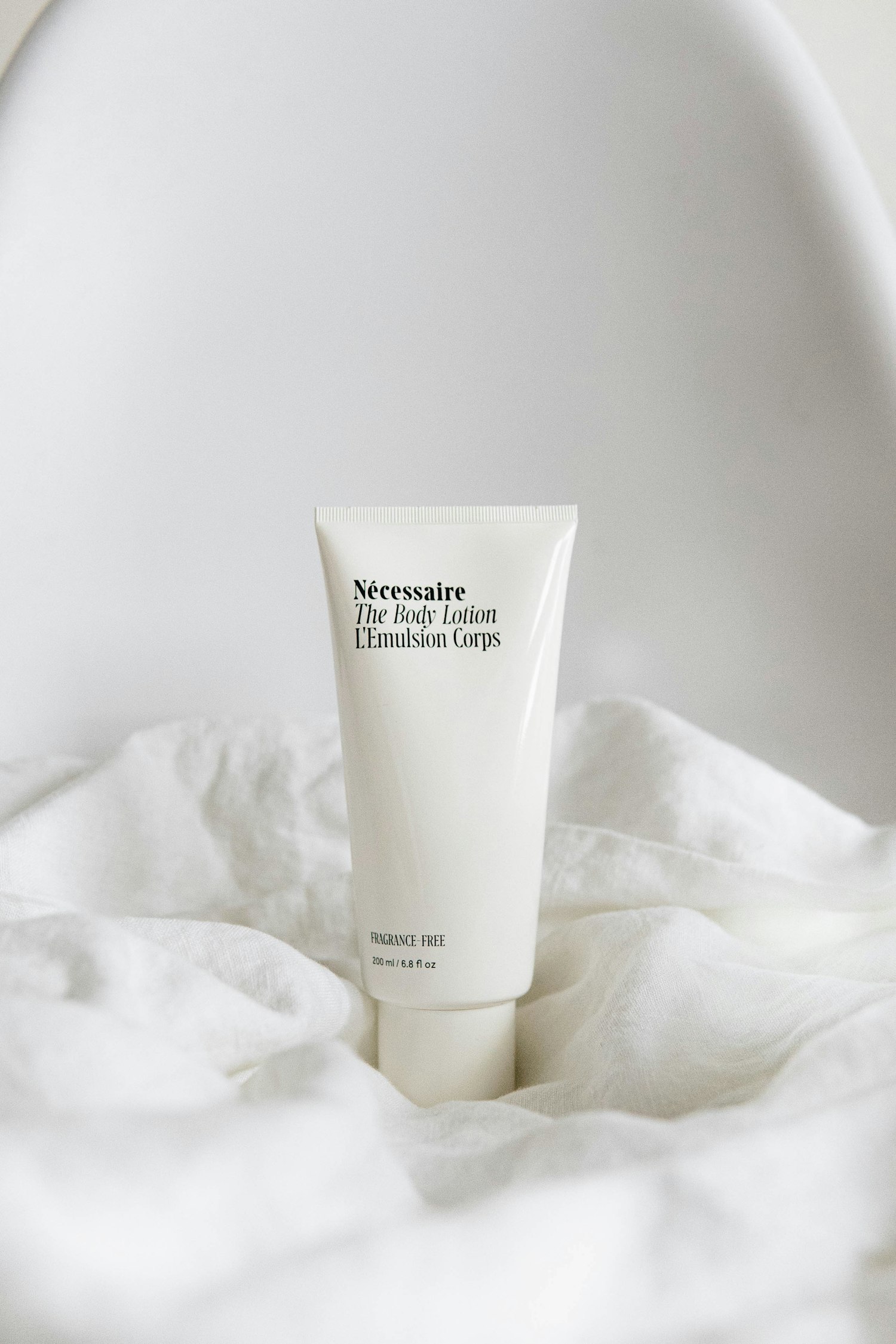 A white tube of fragrance-free body lotion resting on crumpled white linen